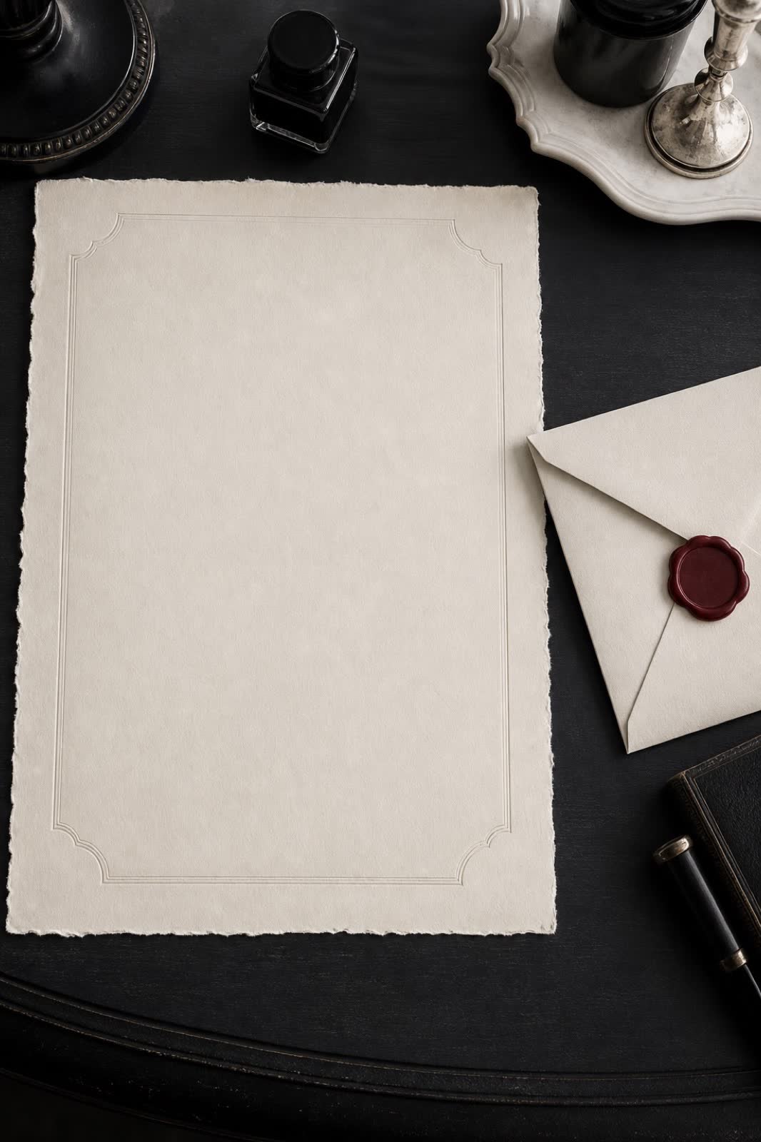 Antique letter paper and ivory envelope with a burgundy wax seal on a black writing desk